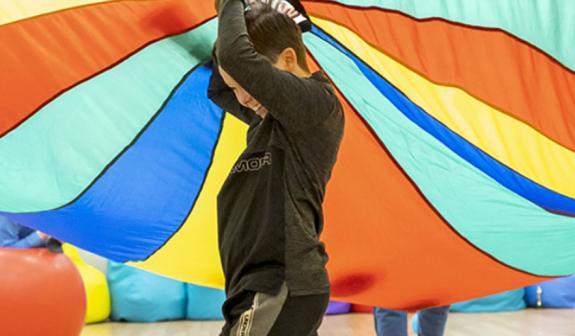 boy underneath a large multi-coloured tent being held by other children